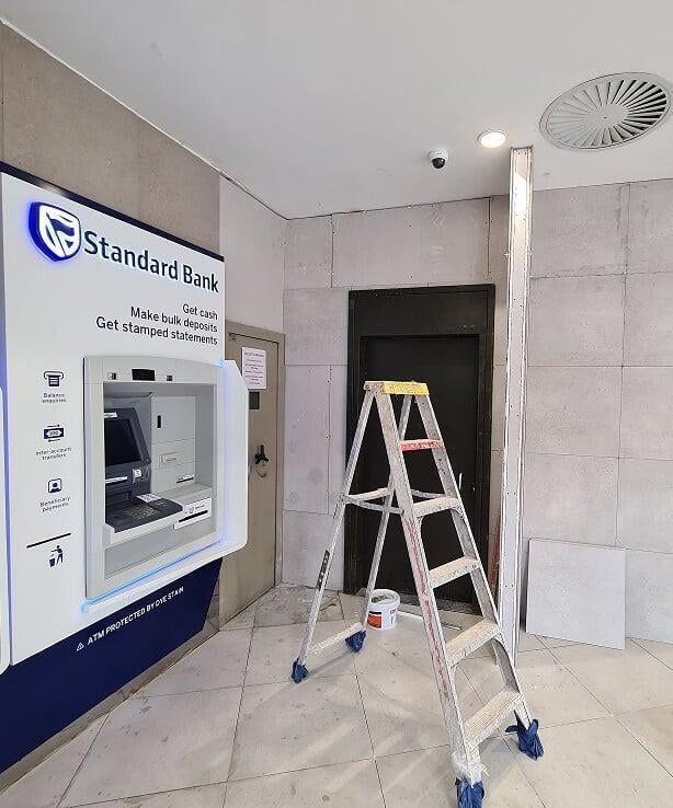 Standard Bank ATM alcove during tiling, with a ladder and a paint tin