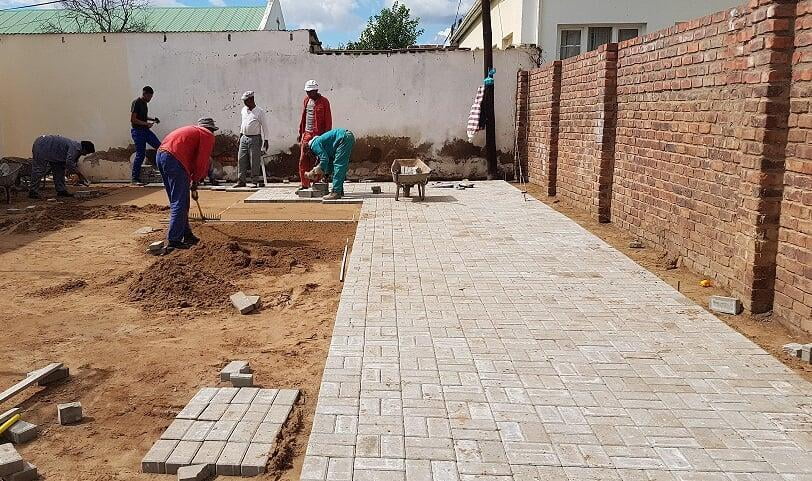 Crew laying a paved walkway beside a brick wall