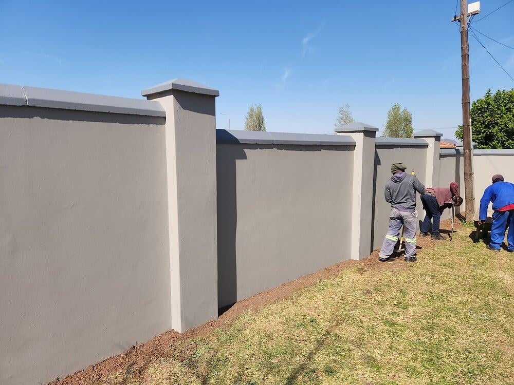 Crew painting a grey boundary wall with pillars
